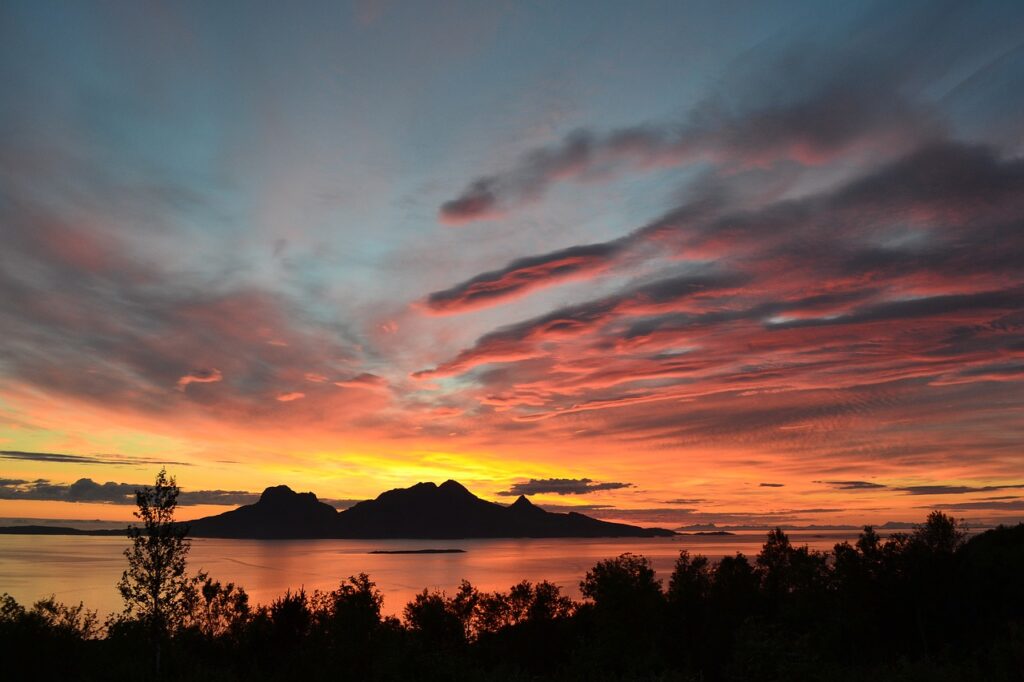 A vibrant sunset over a calm lake with silhouetted mountains.